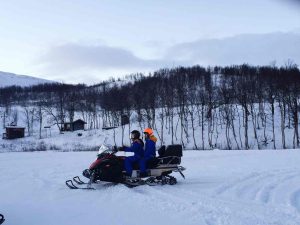 side-view-friends-snowmobiling-snowy-field-against-sky